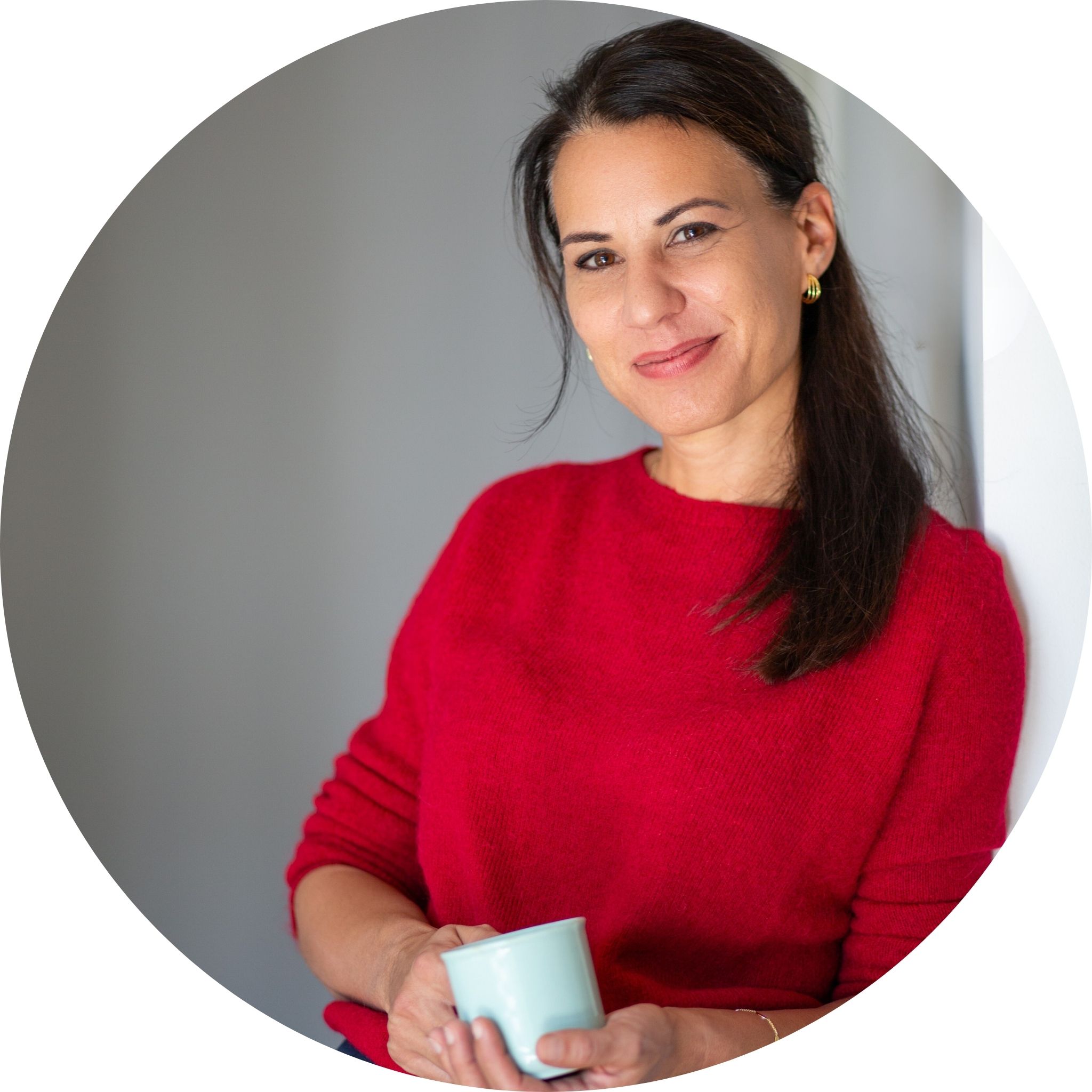 Irene Steindl lehnt mit Kaffeetasse an einer Wand.