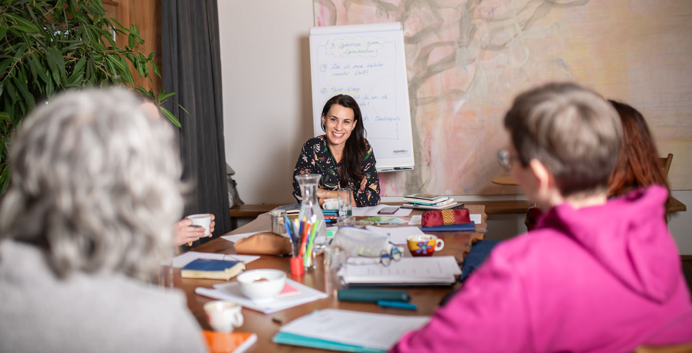 Irene Steindl leitet einen Workshop für mehrere Teilnehmerinnen an einem Tisch mit Flipchart und Arbeitsmaterialien